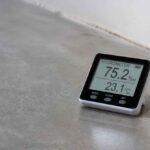 Cyfrowy higrometr pokazujący wilgotność 75,2% i temperaturę 23,1°C na betonowej podłodze