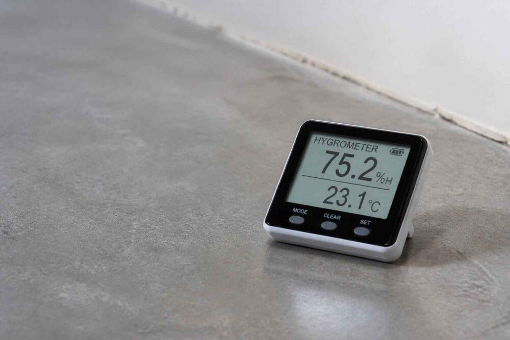 Cyfrowy higrometr pokazujący wilgotność 75,2% i temperaturę 23,1°C na betonowej podłodze