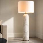 Marmurowa lampa podłogowa obok beżowego fotela w jasnym salonie